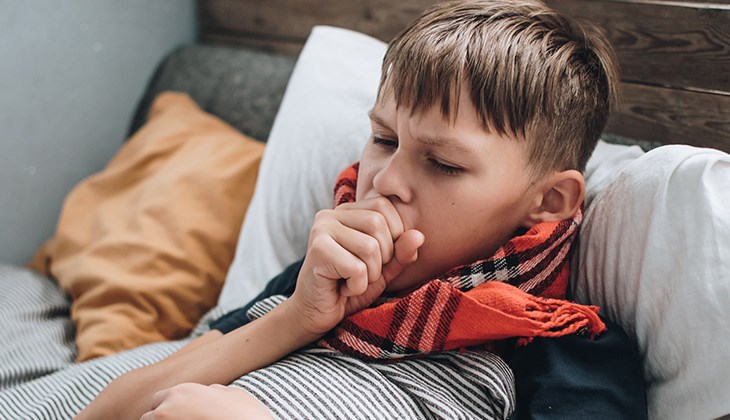 Kranker Junge liegt im Bett mit Schal um den Hals gebunden und hustet