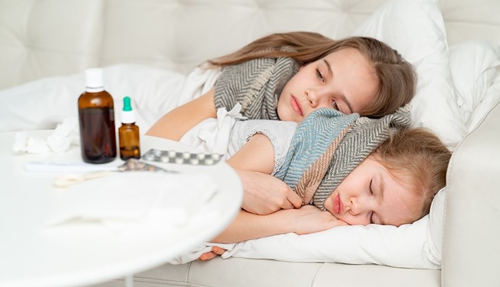 Zwei kranke Mädchen mit Schal um ihren Hals, liegen auf der Couch