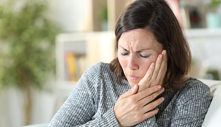 Eine Frau haelt ihre Haende an ihr Gesicht und hat Schmerzen