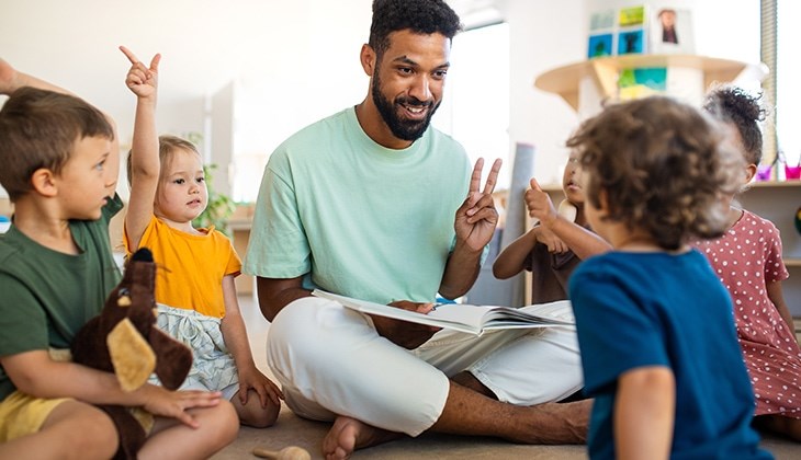 Erzieher sitzt mit Kindern auf dem Boden und übt zählen