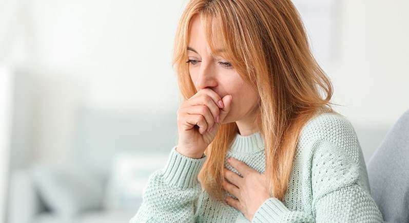 Eine rothaarige Frau in mintfarbenem Pullover hustet