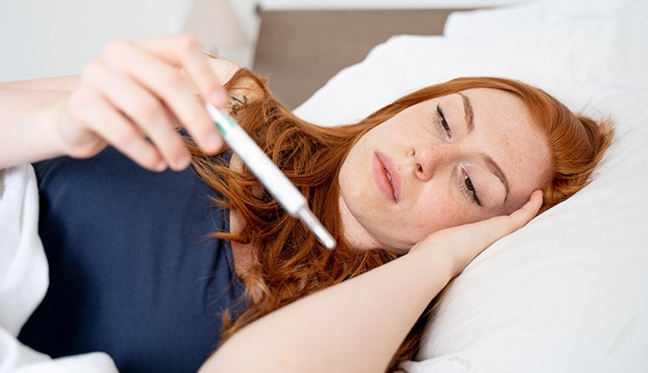 Eine Frau liegt im Bett und misst ihr Fieber