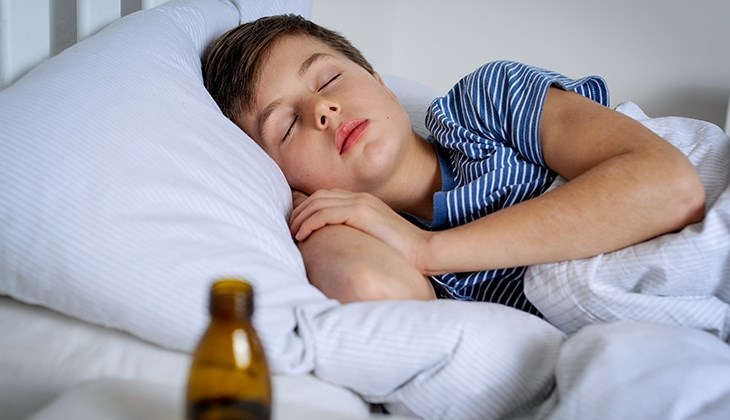 Ein Junge liegt im Bett und schläft. Im Vordergrund sieht man eine Medizinflasche.