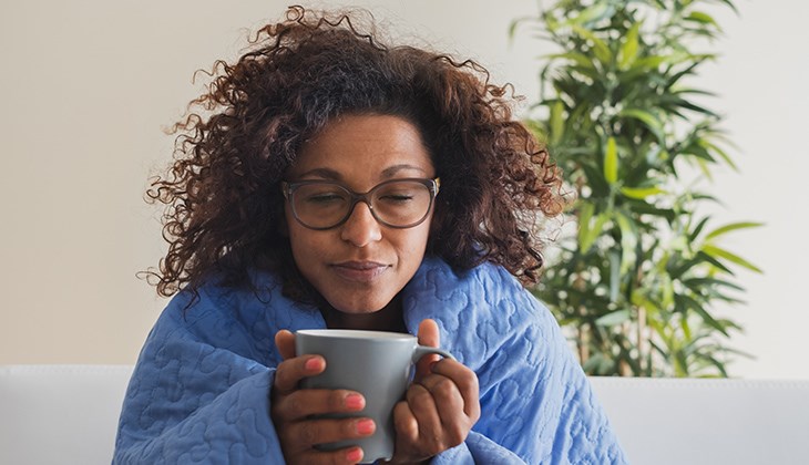 Eine Frau haelt mit beiden Haenden eine Tasse fest