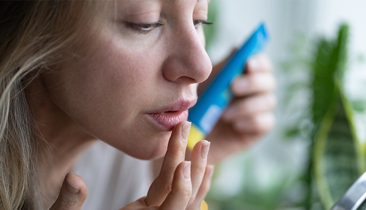 Eine blonde Frau cremt sich die Lippen ein