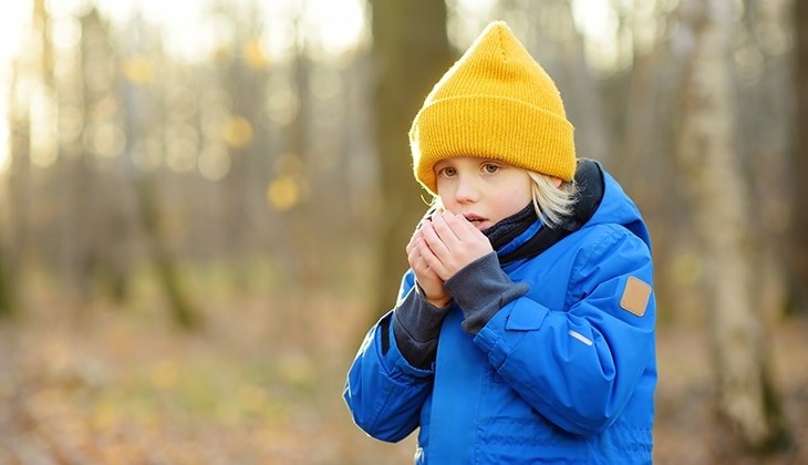 Ein Junge steht dick angezogen im Wald und haucht sich in die Hände