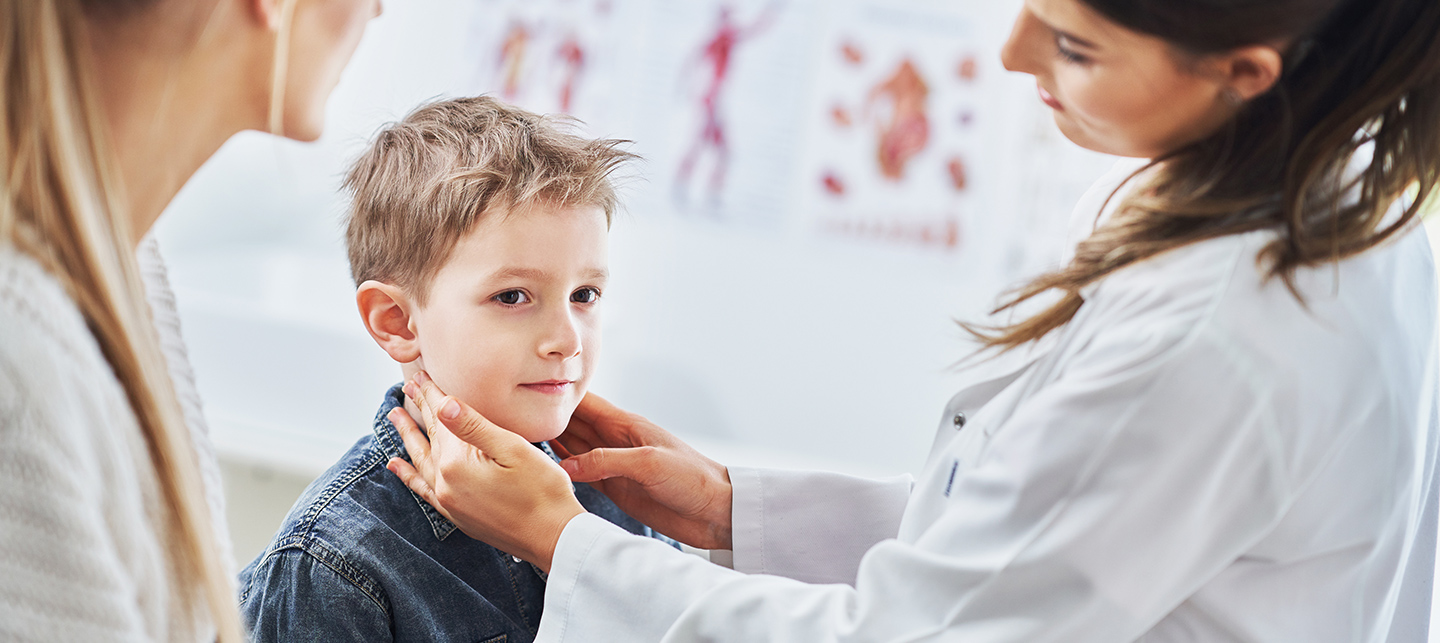 Eine Ärztin tastet bei einem Kind seitlich am Hals nach den Lymphknoten; eine weitere Frau schaut dabei zu.