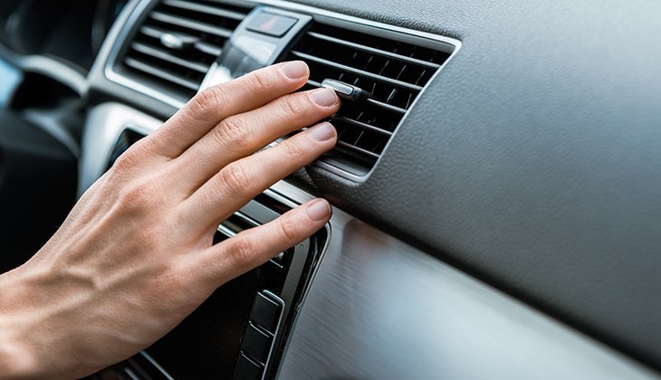 Eine Hand greift nach der Lüftung im Auto und stellt diese ein