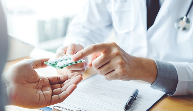 Ein Arzt ueberreicht einer weiteren Person Tabletten