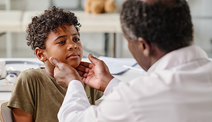 Ein Arzt tastet bei einem jungen Patienten den Hals ab