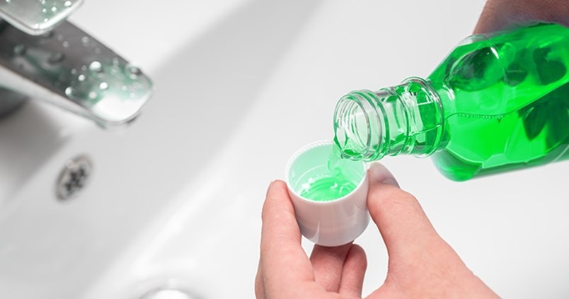 Über einem Waschbecken füllt eine Person Mundspülung in einen kleinen Becher