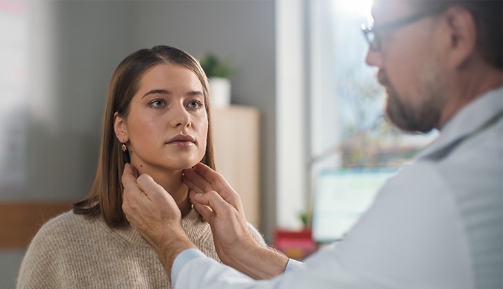 Ein Arzt tastet den Hals einer jungen Patientin ab